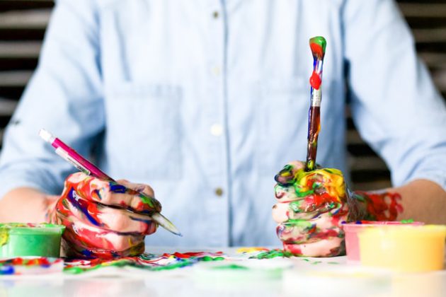 person in button down with paintbrushes covered in paint